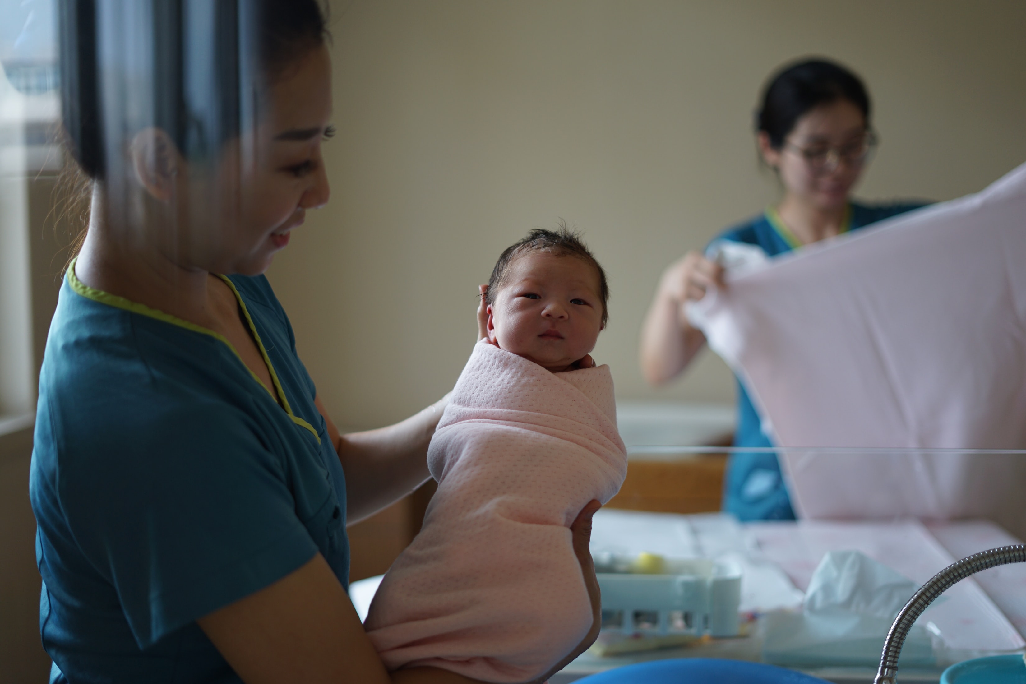 A nurse holding a newborn child swaddled in a blanket.